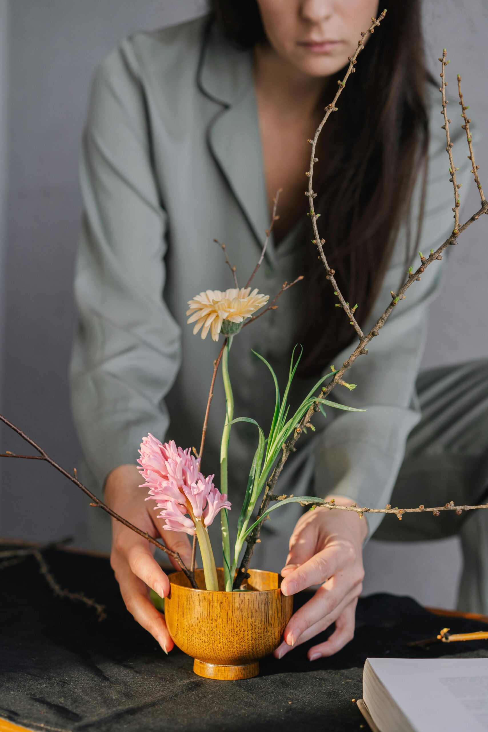 Woman arranging a floral display in a wooden bowl, creating a calm indoor setting.